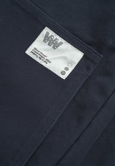 Marine textiel met een geweven structuur, voorzien van een wit gestikt label met een logo, productdetails en was symbolen.