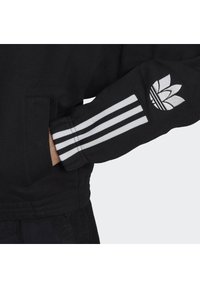 Black sweatshirt with white three-stripe detail on the sleeve and an embroidered logo featuring three leaves on the cuff.