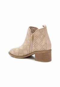 Botín beige hasta el tobillo con suede perforado, cremallera lateral y un tacón de madera apilada. Punta redondeada y detalle de superficie texturizada.