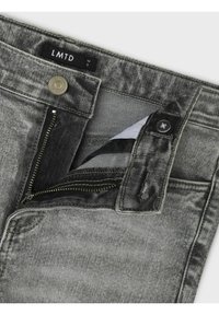 Jeans in denim grigio con chiusura a zip, bottone e etichetta "LMTD." Presentano una texture leggermente consumata e cuciture a contrasto.
