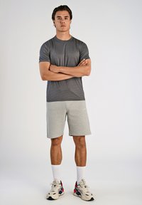 Grå atletisk t-shirt med korte ærmer og lysegrå shorts. Har kontrasterende teksturer og en afslappet pasform. Bæres med hvide sokker og sneakers.