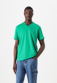 T-shirt vert en V en coton doux, avec des manches courtes et un petit logo sur la poitrine, associé à un jean cargo bleu.