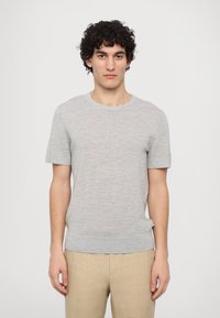 Light grey short-sleeve knit sweater with a round neckline and ribbed hem. Features a textured finish and relaxed fit. Paired with beige trousers.