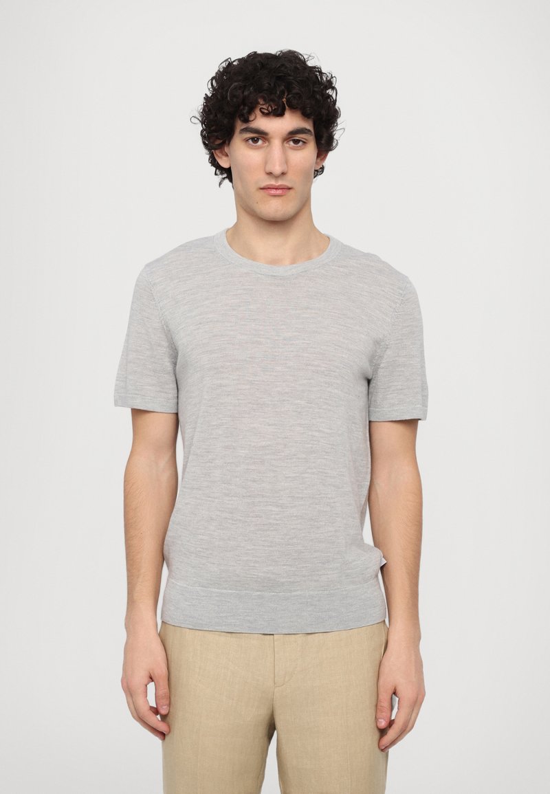 Light grey short-sleeve knit sweater with a round neckline and ribbed hem. Features a textured finish and relaxed fit. Paired with beige trousers.