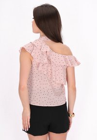 Lyserød bluse med sorte prikker, med en rynket off-shoulder design. Båret med sorte shorts. Glat tekstur og letvægtsstof.