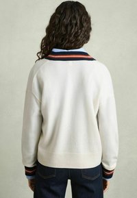 Vit fleece-tröja med marinblå och rostfärgade randiga detaljer vid kragen. Har en ribbad nederkant och en texturerad yta. Buren med mörk denimjeans.