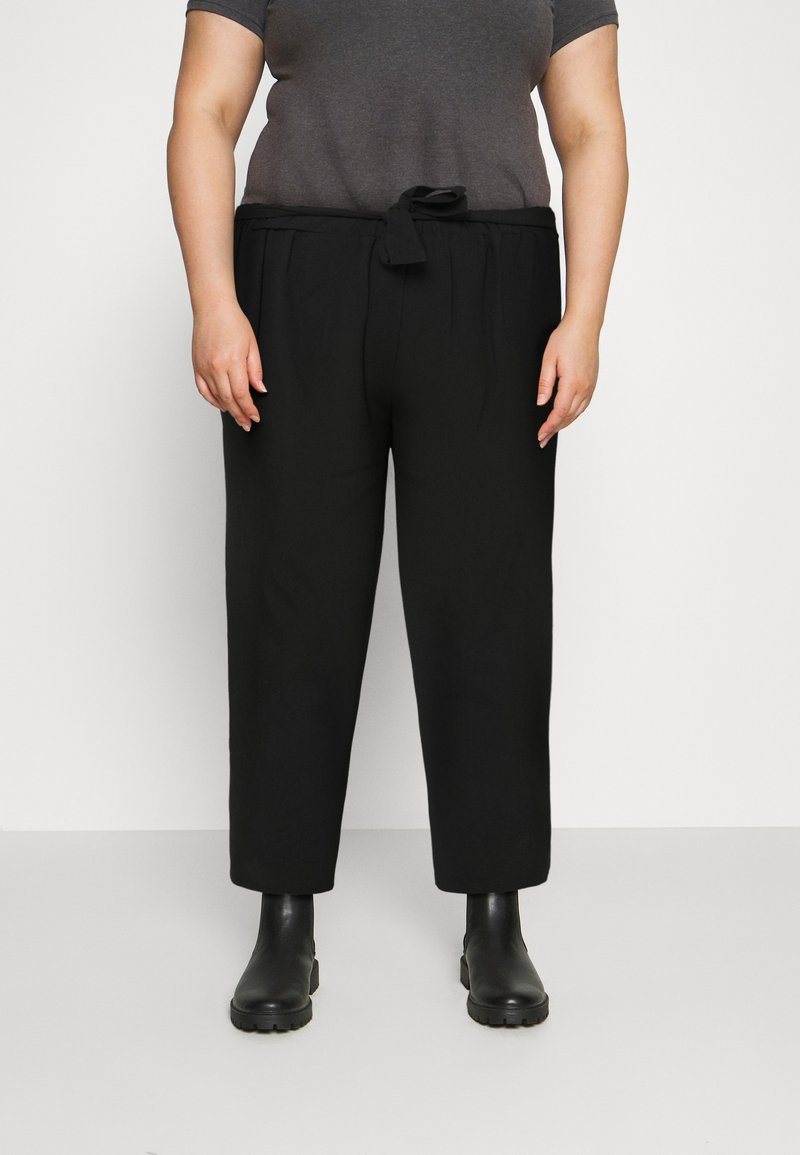 Pantalons noirs, coupés avec un ourlet retroussé et une taille à nouer. Fabriqués dans un tissu lisse, associés à des bottines noires et un haut gris à manches courtes.