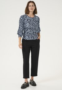 Bluza s uzorkom zebre u plavoj i crnoj boji s balon rukavima, uparena s ravnim crnim hlačama i masivnim crnim loafers cipelama. Jednostavan dizajn, ležeran izgled.