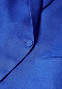 Tissu de blazer bleu avec un bouton unique fermé et détails visibles au niveau du revers et de la poche.