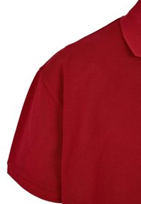 Rød polo-skjorte med strukturert stoff, klassisk krage og korte ermer. Designet inkluderer en løs passform og flat kant.