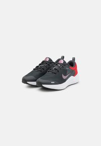 Baskets de sport noires et rouges avec une tige en maille, une semelle rembourrée, des lacets noirs et un logo swoosh rose sur les côtés.