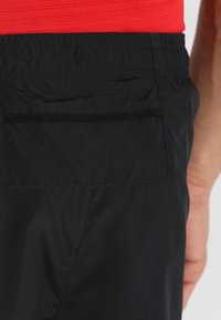Pantalones cortos deportivos negros con una cintura elástica, que cuentan con un bolsillo trasero y una textura de tela ligera y suave.
