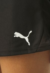 Črne atletske kratke hlače z gladko teksturo, na spodnji levi strani pa je bel logotip Puma, ki prikazuje skočnega mačka.