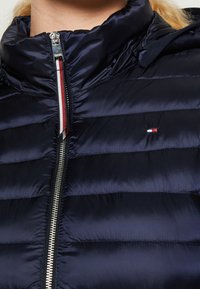 Marineblaue Steppjacke mit hohem Kragen und einem Reißverschluss vorne. Verfügt über horizontal gesteppte Abschnitte, silberne Beschläge und ein Logo-Detail.