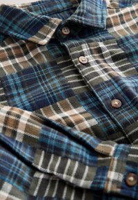 Flannelskjorte med tartanmønster i blå, grøn og brun. Har knappelukning foran og blød tekstur. Brune knapper fremhæver designet.