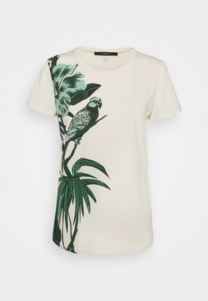 Kermansävyinen lyhythihainen t-paita, jossa vihreitä trooppisia lehtiä ja papukaija oksalla vasemmalla puolella.