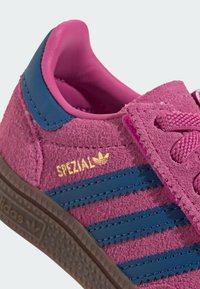 Ljusrosa sneakers i mocka med marinblå ränder, texturerad yta och gummisula. Har en guldfärgad "SPEZIAL"-logga och rosa skosnören.