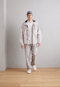 Lightweight, white jacket with black accents, gray beanie, white t-shirt, and light gray sweatpants, paired with white sneakers.