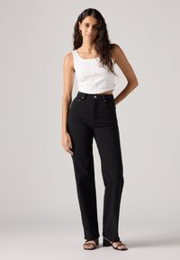 Zwarte high-waisted jeans met een recht model en vijf-pocketstijl, gecombineerd met een fitted witte cropped tanktop.