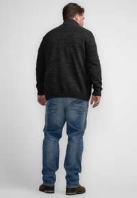 Suéter de punto carbón con cuello alto, puños y dobladillo acanalados, combinado con jeans azul claro y botas marrones, visto desde atrás.