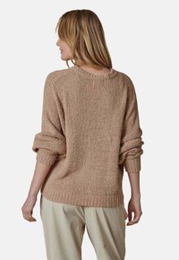Beiger Strickpullover mit lockerer Passform, weitem Ausschnitt und umgeschlagenen Ärmeln, kombiniert mit lässigen, hellen Ripp-Hosen.