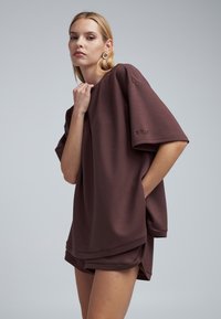 Bruine oversized sweatshirt gemaakt van zacht materiaal met korte mouwen. Heeft een losse pasvorm en zichtbare stikseldetails. Shorts in bijpassende kleur.