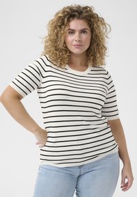 Tricou cu mânecă scurtă, cu dungi orizontale negre pe un fundal crem, având guler rotund și o textură moale. Este purtat cu blugi de culoare albastru deschis.