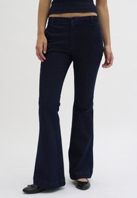 Dark denim flared pants with a fitted waist, front pockets, and clean stitching. Fabric has a smooth texture and subtle vertical lines.