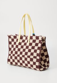 Borsa a tracolla all'uncinetto con un motivo a scacchi marrone e crema, dotata di manici in pelle gialla e dettagli decorativi blu.