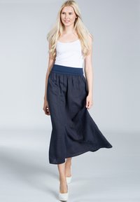 Marineblaue Leinen-Maxikleid mit einem breiten elastischen Bund, fließendem Saum und lässiger Passform, kombiniert mit einem weißen Tanktop und weißen High Heels.