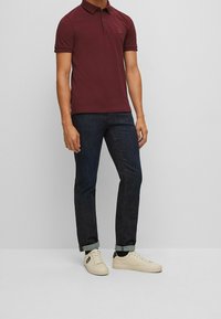 Burgundy polo skjorta med krage, korta ärmar och en liten logotyp. Matchad med mörk denim jeans och krämfärgade sneakers. Enkelt design.