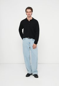 Czarna, długorękawowa koszulka polo z kołnierzykiem i kieszonką, zestawiona z jasnoniebieskimi, szerokimi spodniami dżinsowymi i czarnymi butami. Gładkie kolory, casualowy krój.