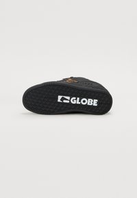 Black skate shoe with a textured rubber sole, featuring a white "GLOBE" logo and detailed stitching on the upper.