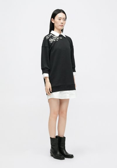 Μαύρη φούτερ μπλούζα με λουλουδάτη κεντητή διακόσμηση στον ώμο, συνδυασμένη με λευκό γιακά πουκαμίσ�ου και λευκή φούστα, συμπληρωμένη με μαύρες γαλότσες αστραγάλου.