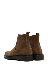 Botas Chelsea de ante marrón con paneles laterales elásticos, punteras redondas y suelas de goma texturizadas. Detalles cosidos alrededor de las costuras.