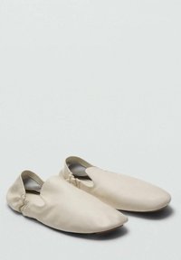 Beżowe buty wsuwane wykonane z gładkiej tkaniny, z zaokrąglonym noskiem, elastycznym otworem i płaską podeszwą. Minimalistyczny design bez widocznych elementów metalowych.