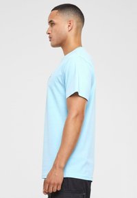 T-shirt en coton bleu clair avec des manches courtes et un col rond, présentant un design graphique sur la poitrine et une coupe décontractée.