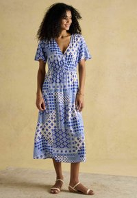 Maxi-Kleid mit blau-weißem Muster, kurzen Ärmeln, V-Ausschnitt, elastischem Bund und einem schwingenden Rock. Kombiniert mit leichten Sandalen.