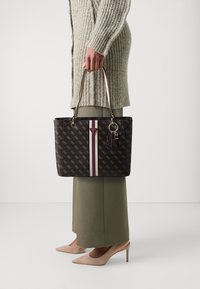 Sac fourre-tout noir avec des rayures verticales crème et bordeaux ; comprend un charm en argent et des poignées robustes ; fabriqué en matériau synthétique texturé.