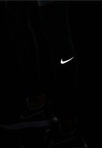 Leggings sportivi neri con un logo Nike bianco riflettente a forma di swoosh sulla parte bassa della gamba. Il tessuto sembra elastico e aderente.