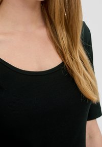 Svart ribbad topp med rundad halsringning och korta ärmar, som visar en mjuk tygtextur med subtil stretch.