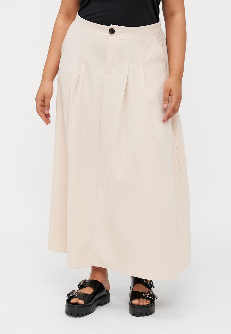 Μπεζ, ελαφρύ, φούστα Α-γραμμής με πτυχές, μπροστινό κλείσιμο με κουμπιά και πλαϊνές τσέπες; συνδυασμένη με μαύρες πλατφόρμες σανδάλια που διαθέτουν διακοσμητικά στοιχεία.