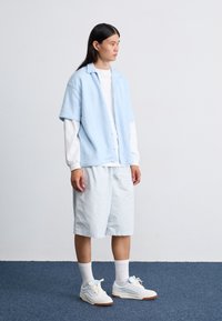 Light blue short-sleeve button-up shirt over a white long-sleeve shirt, paired with light blue shorts and white sneakers with blue accents.