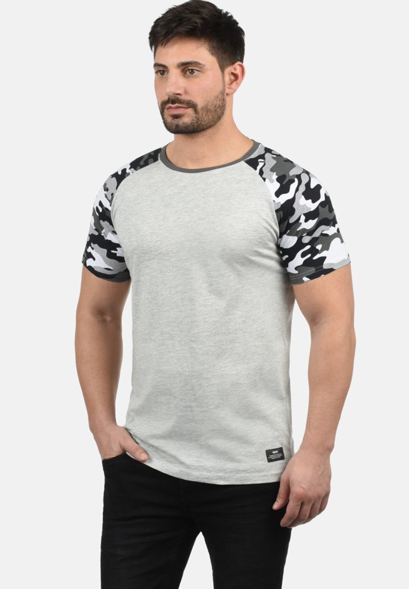 Grå kortermet t-skjorte med ensfarget kropp og camouflagemønstrede ermer. Har rund hals og et lite logomerke ved kanten.