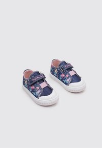 Zapatos de mezclilla azul con patrones florales, acentos rosas y correas de Velcro elásticas. Suela de goma con un patrón de corazones rosas. Diseño de caña baja.