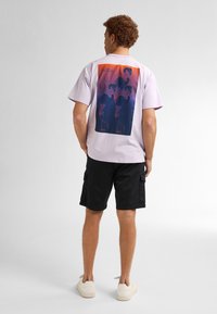 Paarse T-shirt met korte mouwen met een grafisch ontwerp op de achterkant, gecombineerd met zwarte cargoshorts en lichte sneakers.