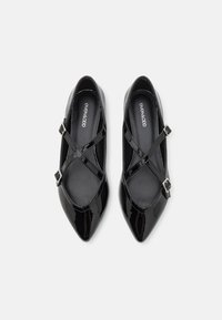 Zapatos Mary Jane de charol negro con puntera afilada, correas cruzadas y detalle de hebilla plateada. Textura suave con un acabado brillante.