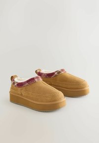 Tan suède instap schoenen met een dikke rubberen zool, voorzien van een luxe witte voering en een rode geruite accent rond de kraag.