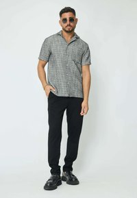 Chemise à motifs noir et blanc à manches courtes avec des boutons, associée à un pantalon slim noir et des mocassins noirs, présentée dans un design décontracté.