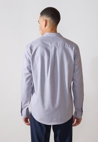 Camicia a maniche lunghe con tessuto a fantasia azzurro chiaro, polsini con bottone e orlo arrotondato, vista da dietro.